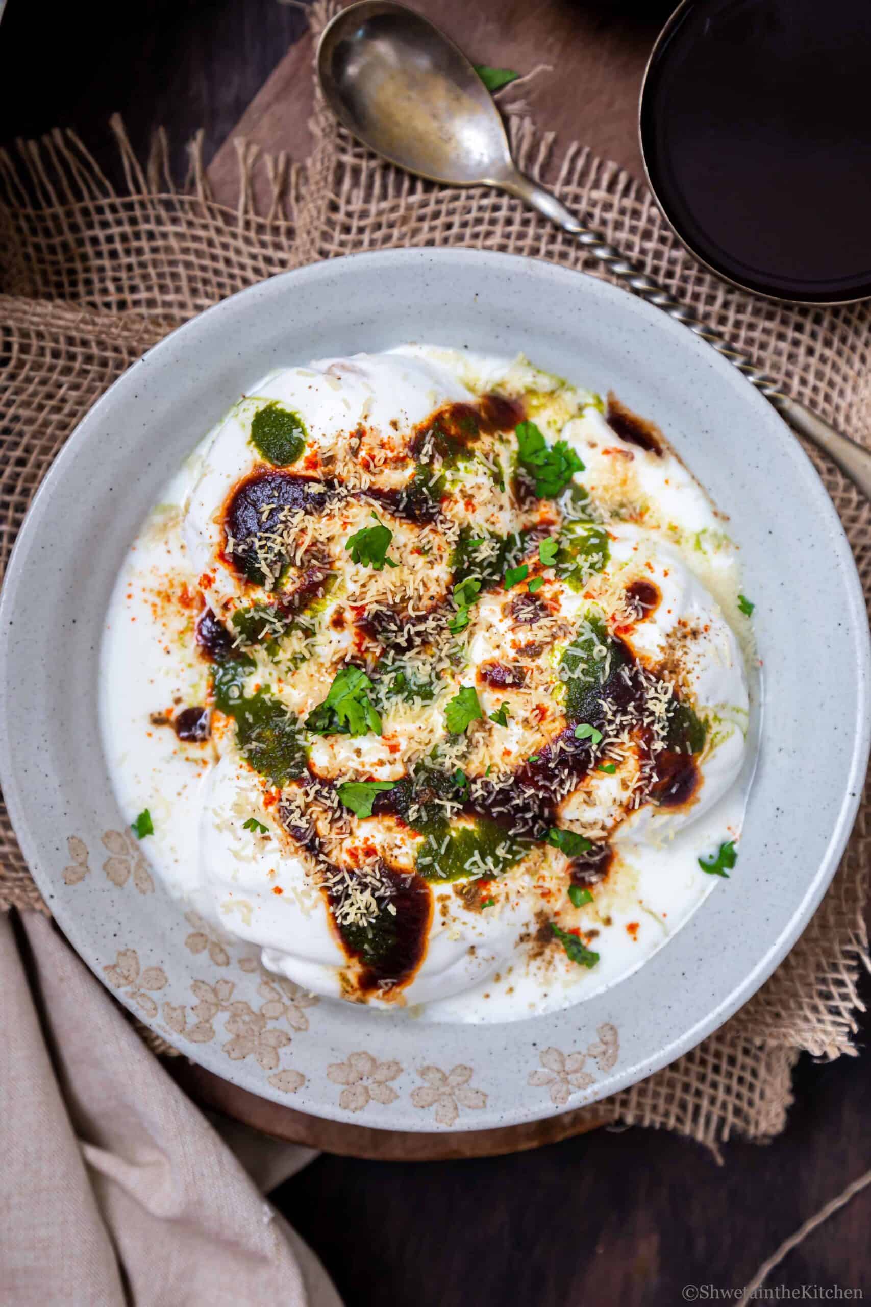Dahi Vada (Dahi Bhalla) served on a white plate with sweet and spicy chutneys. 
