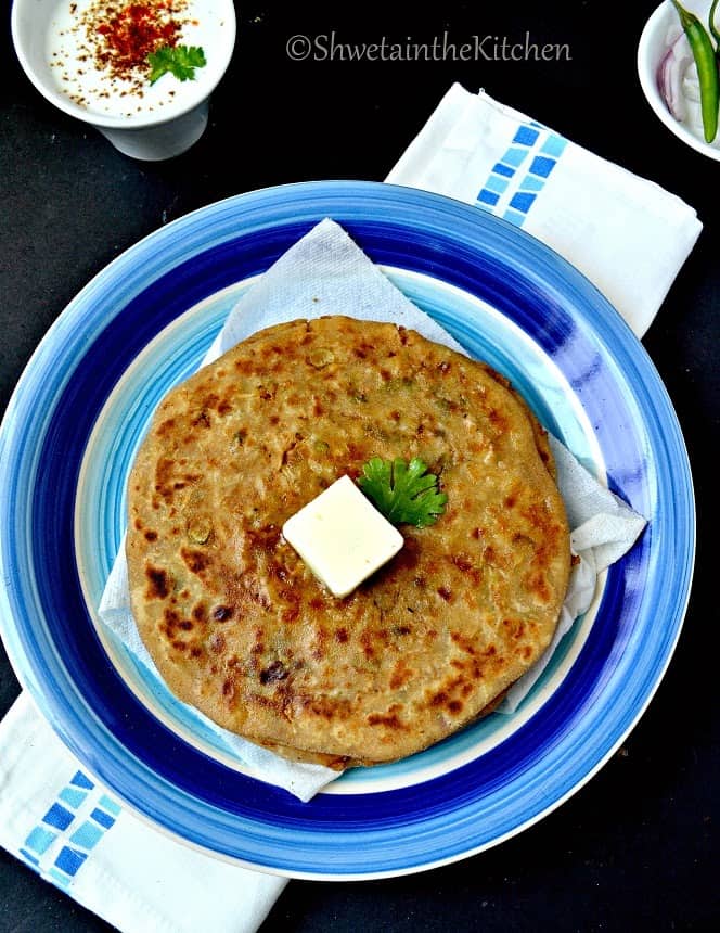 Overhead shot of mooli paratha served on a plate with fresh herbs and butter.