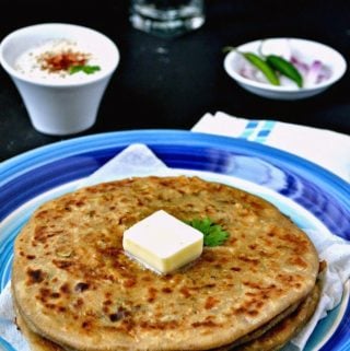 A stack of mooli paratha served on a plate and topped with a pat of butter.