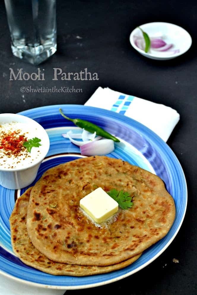 Two stuffed parathas on a blue plate served with raita.