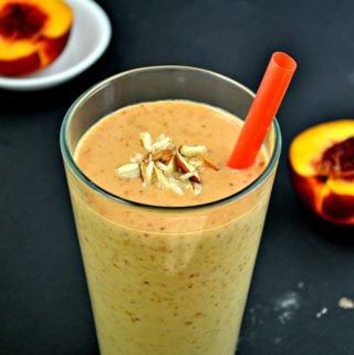 A nectarine smoothie in a glass with a straw and topped with almond pieces