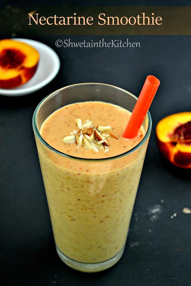 A nectarine smoothie in a glass with a straw and topped with almond pieces
