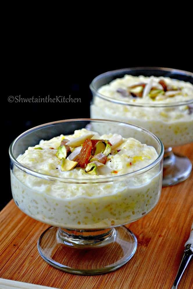 Rice pudding served in two glass bowls and topped with dried fruits and pistachios