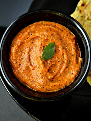 Tomato chutney in a black bowl with curry leaf on top
