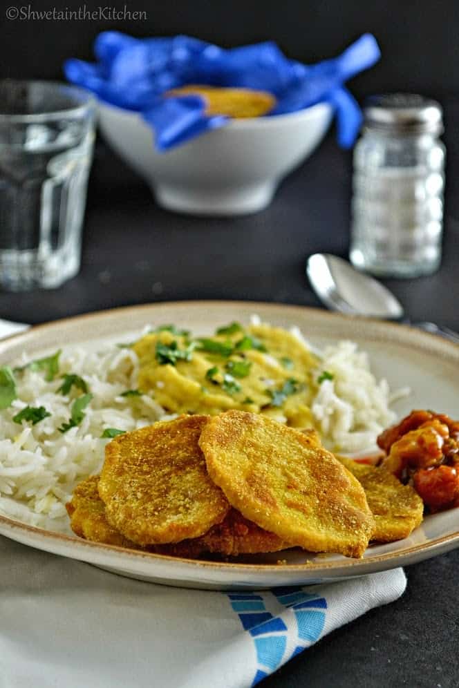 The Indian potato slices served with dal and pickle on a white plate