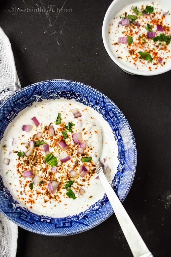 A spoon in a bowl of raita topped with red onions