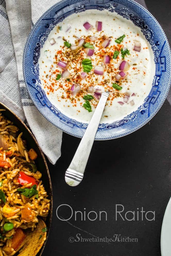 Creamy Indian yogurt served in a bowl and topped with red onions and spices