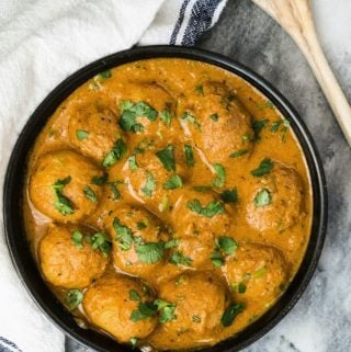 Dum aloo in a skillet garnished with cilantro next to a wooden spoon