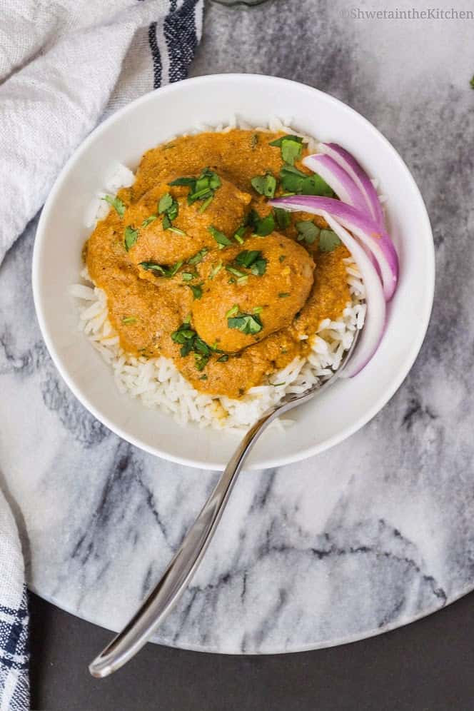 The potato curry served over rice and garnished with red onion slices and herbs