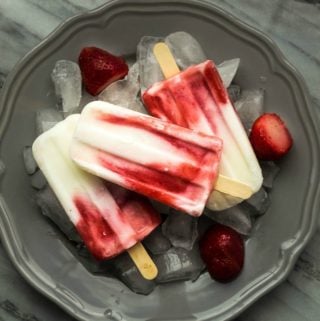 Three strawberry and yogurt popsicles on a grey plate