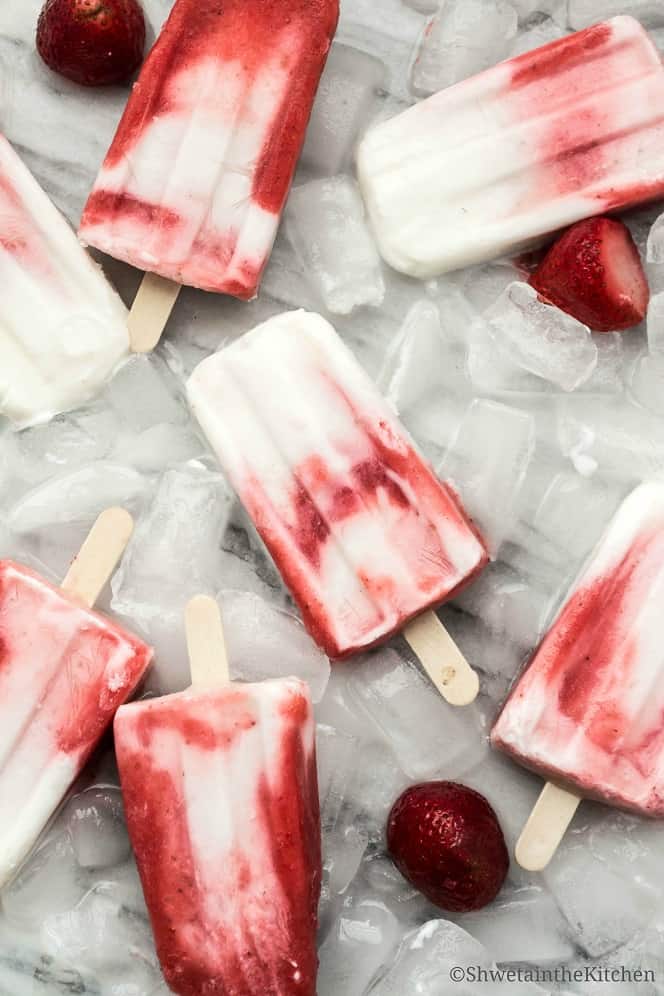 Strawberry yogurt popsicles laying on ice cubes