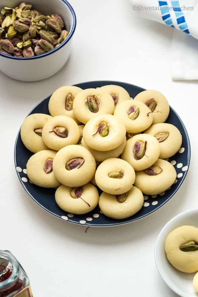 Milk Pedas decorated with pistachios served on a blue patterned plate