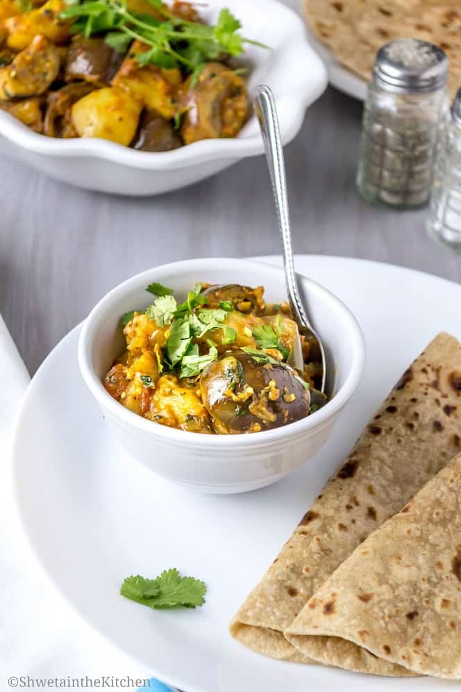 A spoon in a bowl of the eggplant and potato curry served with Indian flatbread