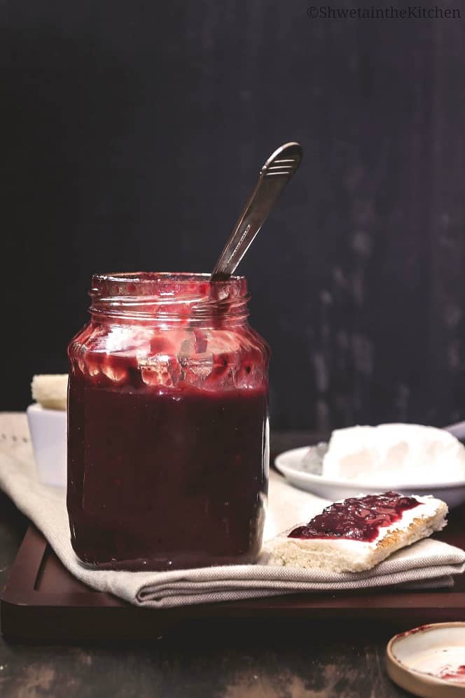Plum chutney in a jar on a cutting board next to a piece of toast