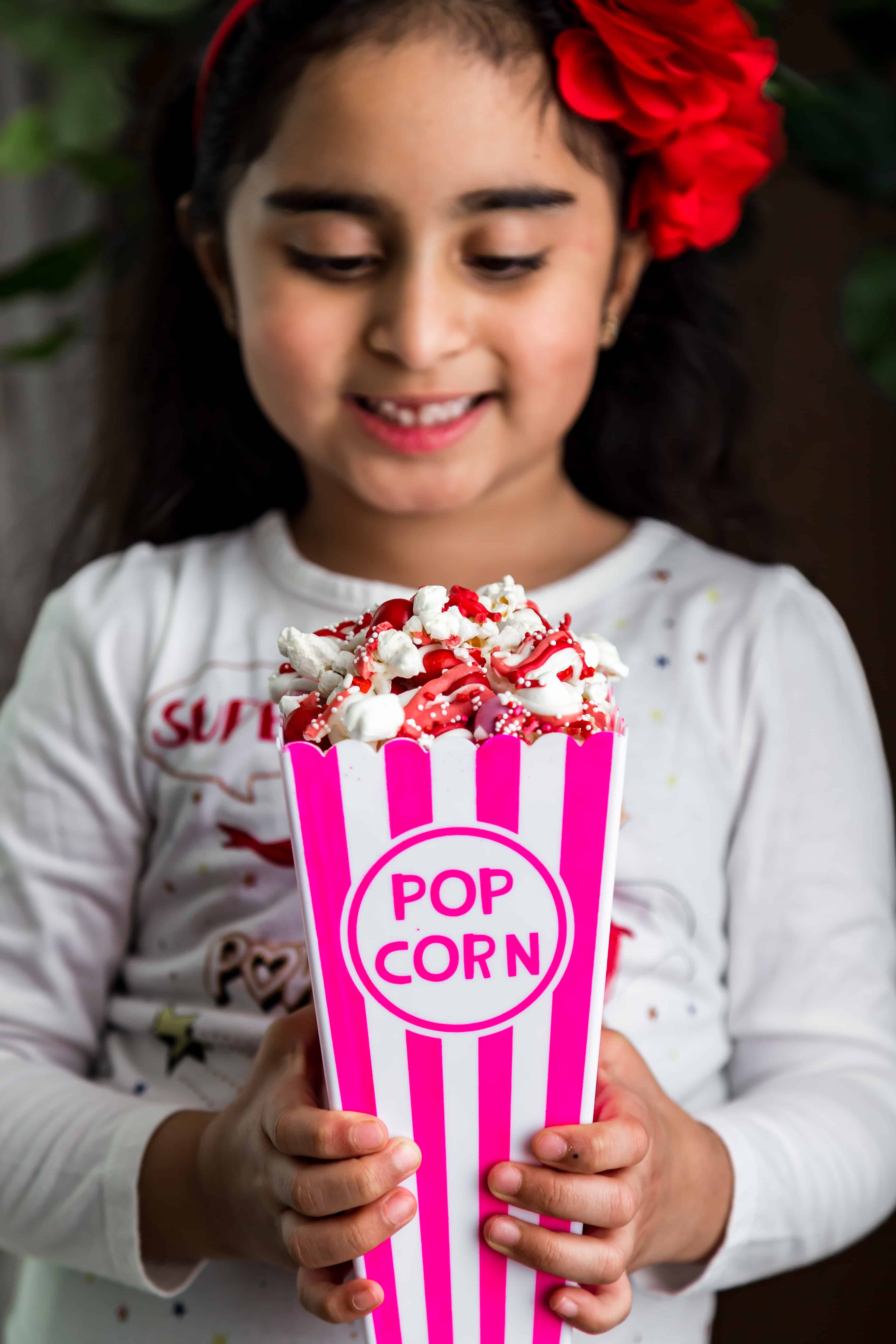 A girl smiling and looking at the popcorn container of Chocolate Drizzled Popcorn in her hand. 