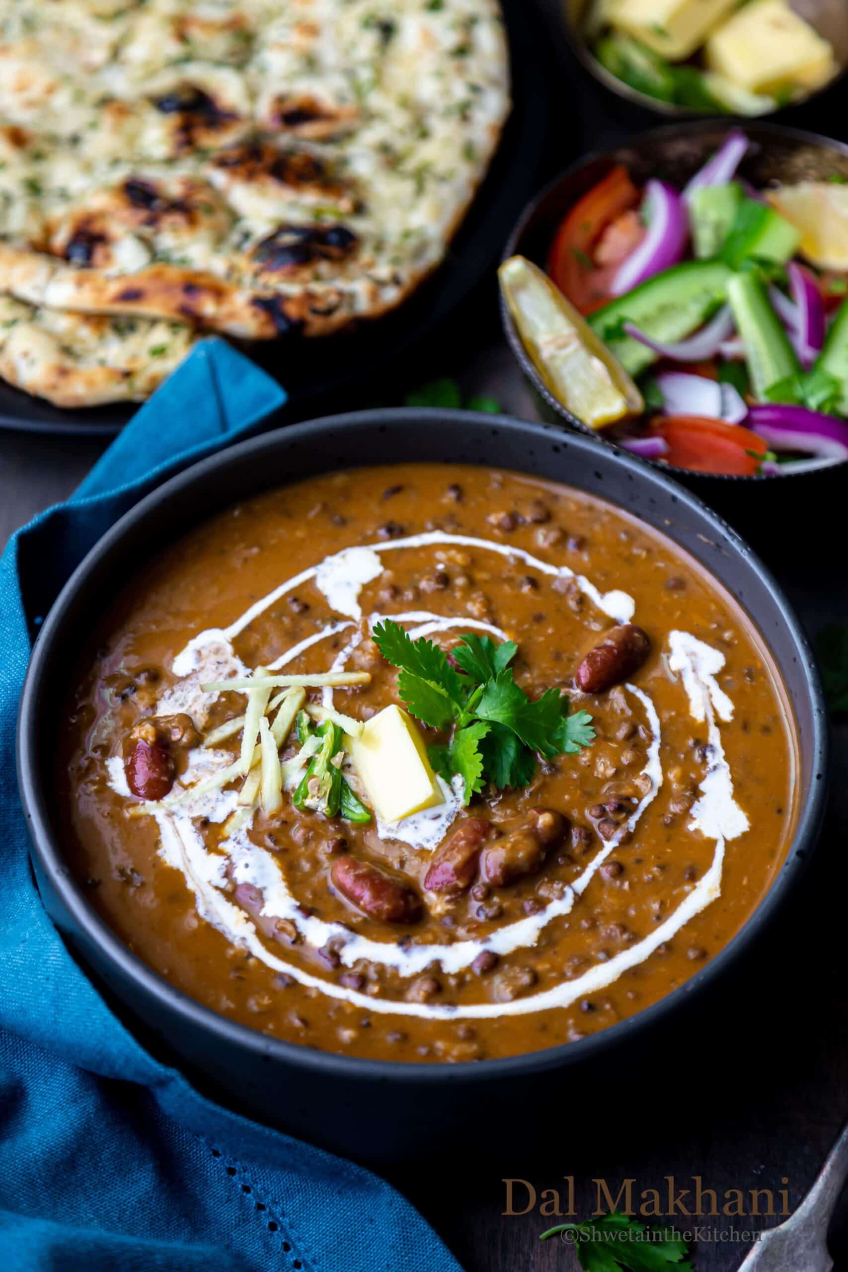 Dal Makhani in a black bowl with salad and naan on side