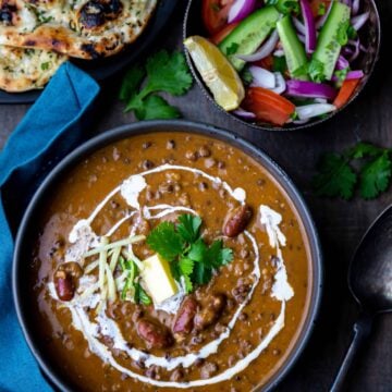 Punjabi Dal Makhani in a black bowl with salad bowl and naan on side