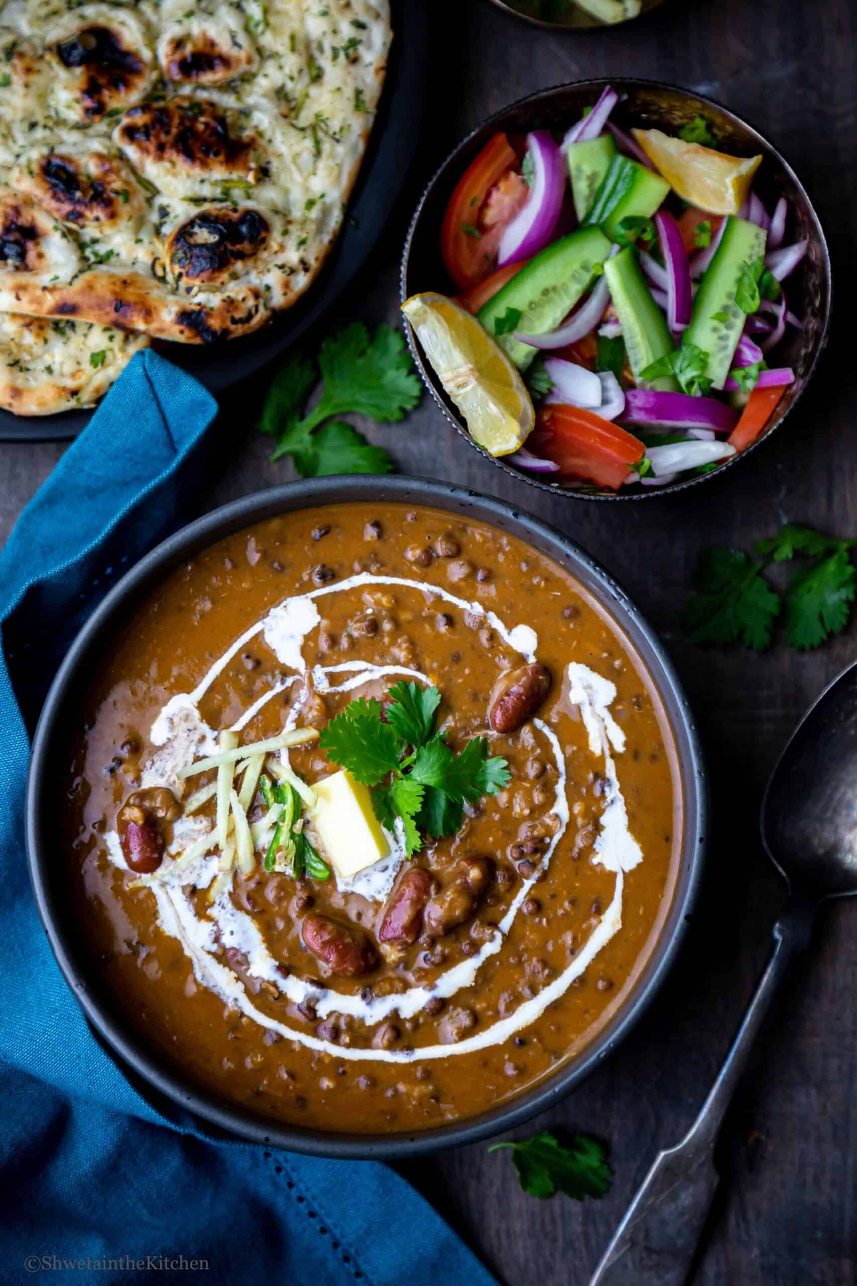 Punjabi Dal Makhani in a black bowl with salad bowl and naan on side 