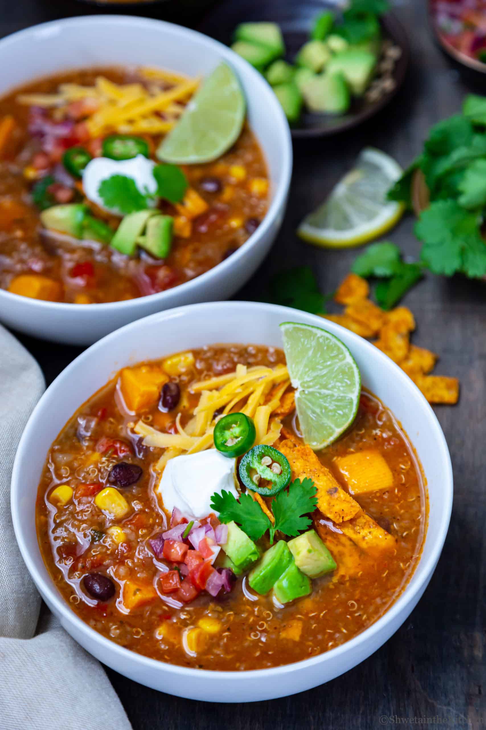 two white bowls of Vegetarian Enchilada Soup with toppings, cheese and lime.