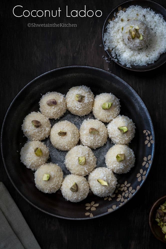 Coconut Ladoo on a plate garnished with pistachios and one ladoo on the side dipped in desiccated coconut.