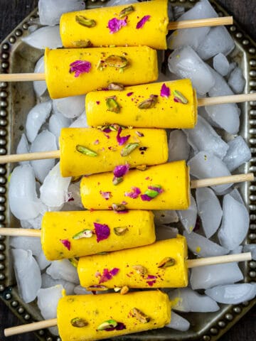 8 Mango Kulfis on a ice filled tray topped with pistachios and dry rose petals