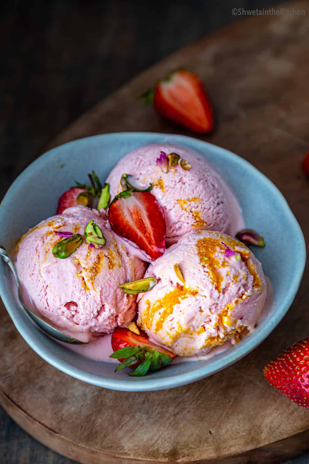 three scoops of strawberry ice cream in a blue bowl garnished with cut strawberry and pistachios. 