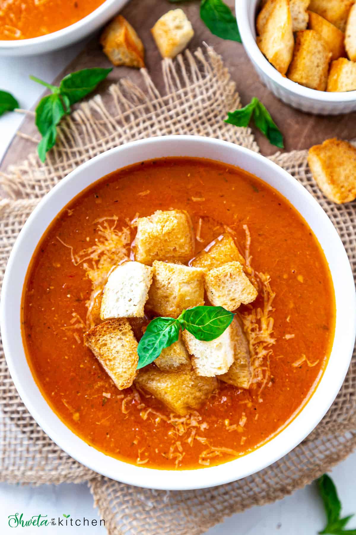 Bowl of Tomato basil soup with crouton and basil leaves placed on burlap cloth