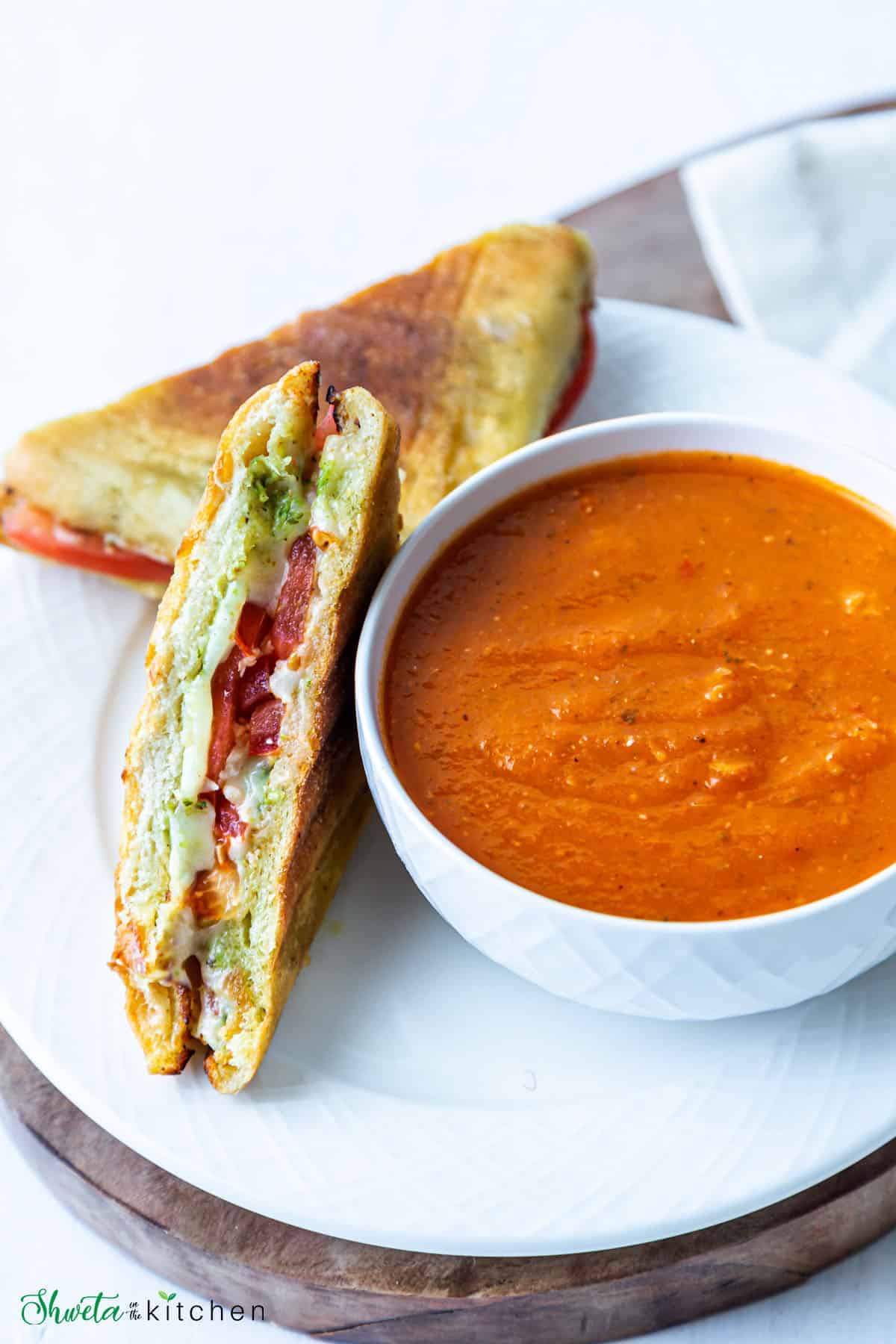 Tomato basil soup in a bowl with grilled cheese sandwich on side on a plate