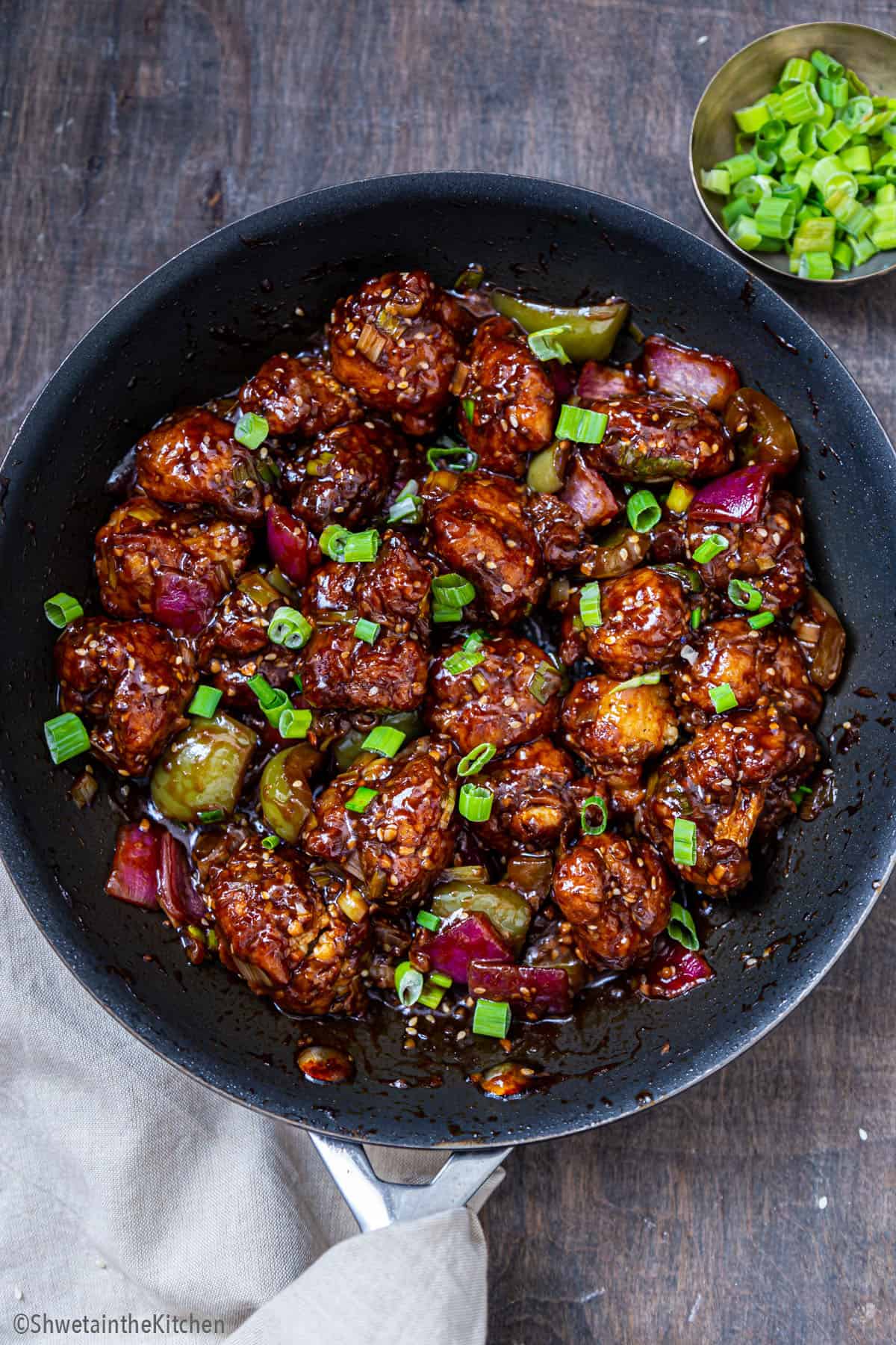 Gobi Manchurian in a wok with spring onions green at the side
