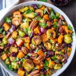 Bowl of roasted brussels sprouts and sweet potatoes with bowl of dry cranberries at side