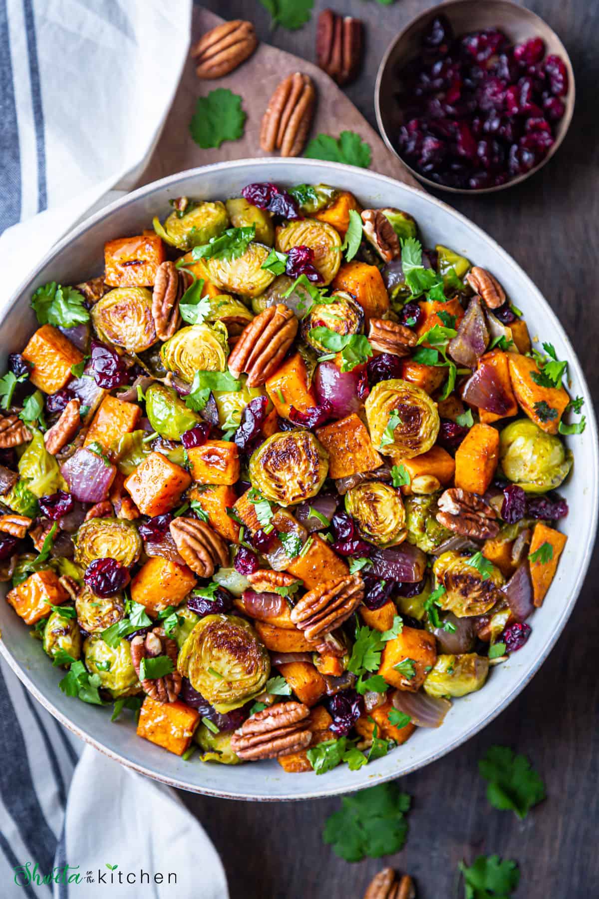 Bowl of roasted brussels sprouts and sweet potatoes with bowl of dried cranberries at side