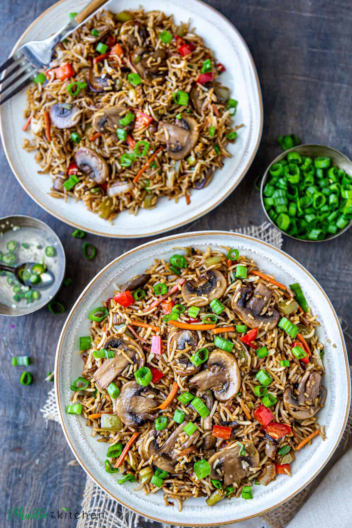 Two plates of mushroom fried rice with spring oniongreens and chilli vinegar on side