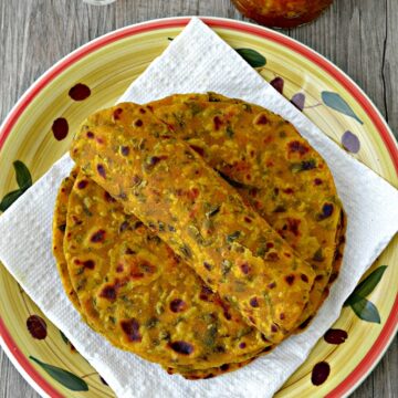 Methi thepla rolled on stack of theplas placed on white tissue lined plate