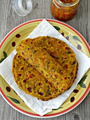 Methi thepla rolled on stack of theplas placed on white tissue lined plate