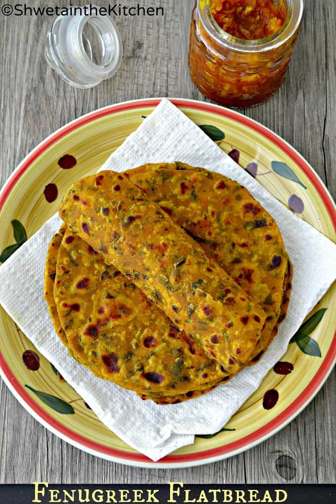 Methi thepla rolled on stack of theplas placed on white tissue paper lined plate