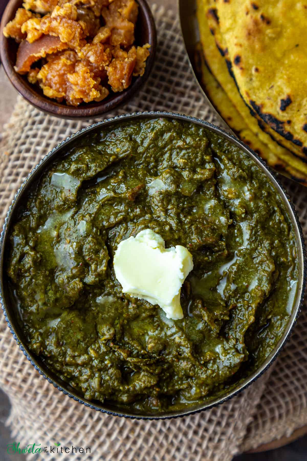 Sarson ka Saag in a bowl topped with white butter and makki ki roti and gud (jaggery) on the side