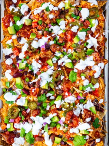 Veg Nachos on a baking tray topped with diced avocado, sour cream and salsa.