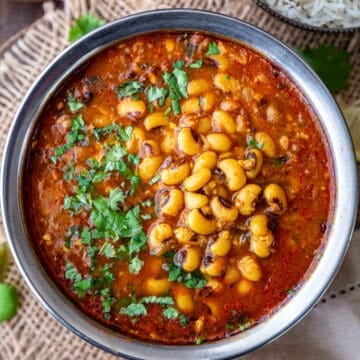 Lobia (black eyed peas) curry in a bowl on a wooden surface with rice and salad on the side