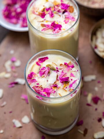 Thandai in two glasses topped with dry rose petals and sliced almonds
