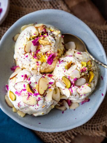 three scoops of thandai ice cream garbished with sliced almonds and dried rose petals in a blue bowl
