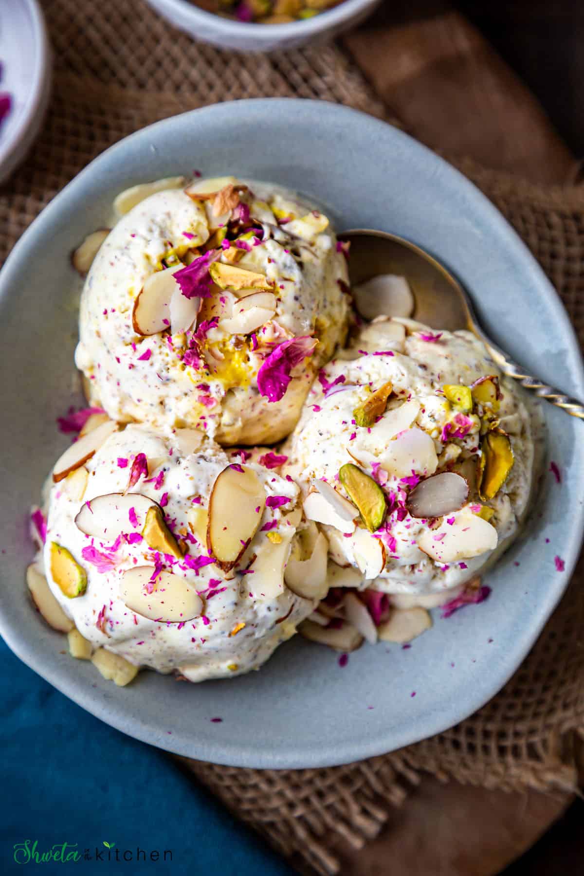 three scoops of thandai ice cream garnished with sliced almonds and dried rose petals in a blue bowl
