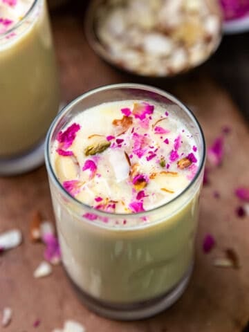 Thandai in a glass topped with dry rose petals and sliced almonds