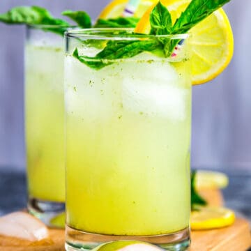 Front view of two glasses of basil ginger lemonade garnished with lemon and basil leaves
