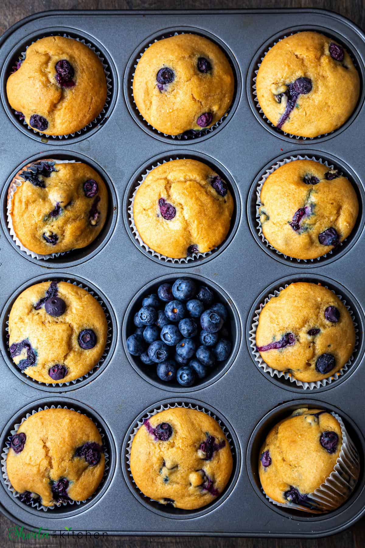 Muffin tray filled with blueberry muffins and one just with blueberries