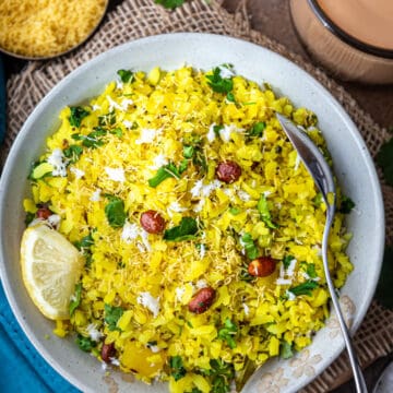 Plate of Poha garnished with cilantro, coconut and sev witth chai on side