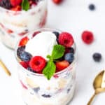 Side view of berry parfait topped with cream and mint and golden spoon on side