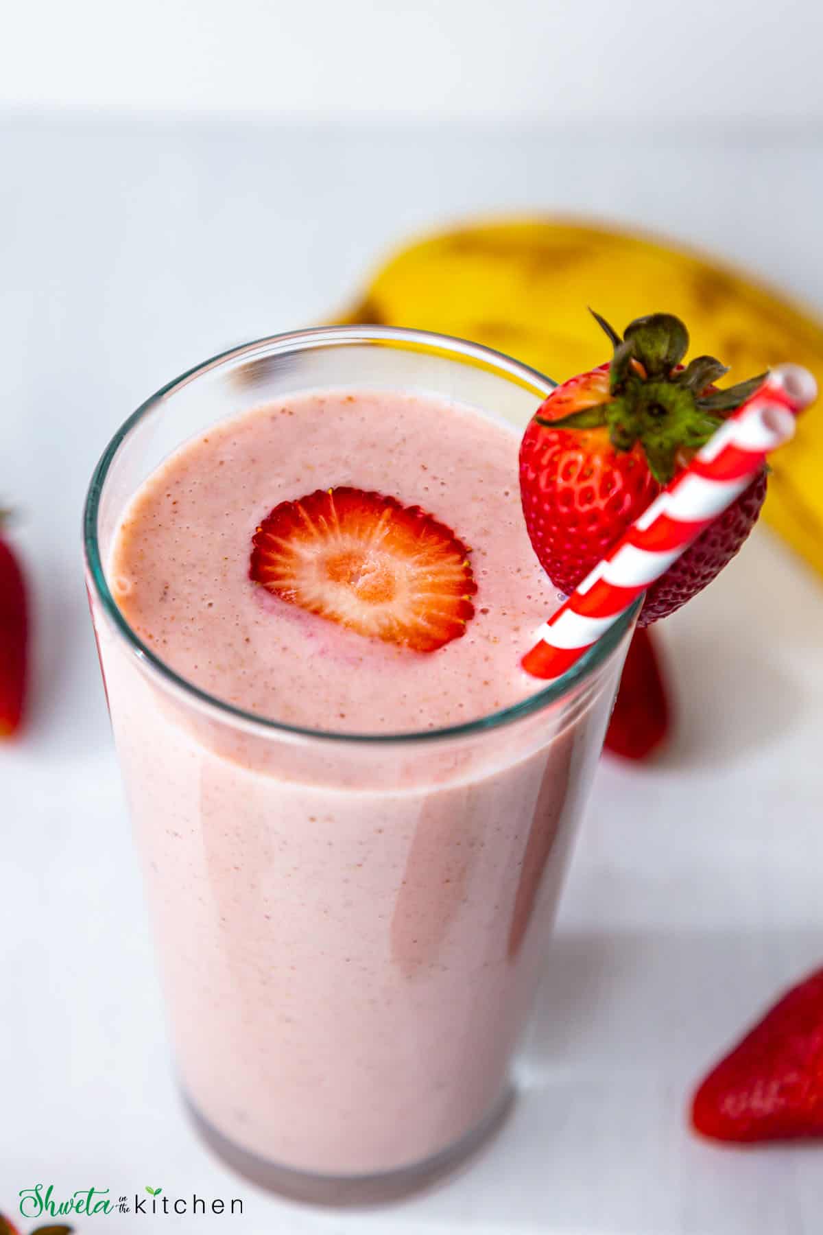 Strawberry banana smoothie in a tall glass with red stripped straw and strawberry on the side and centre
