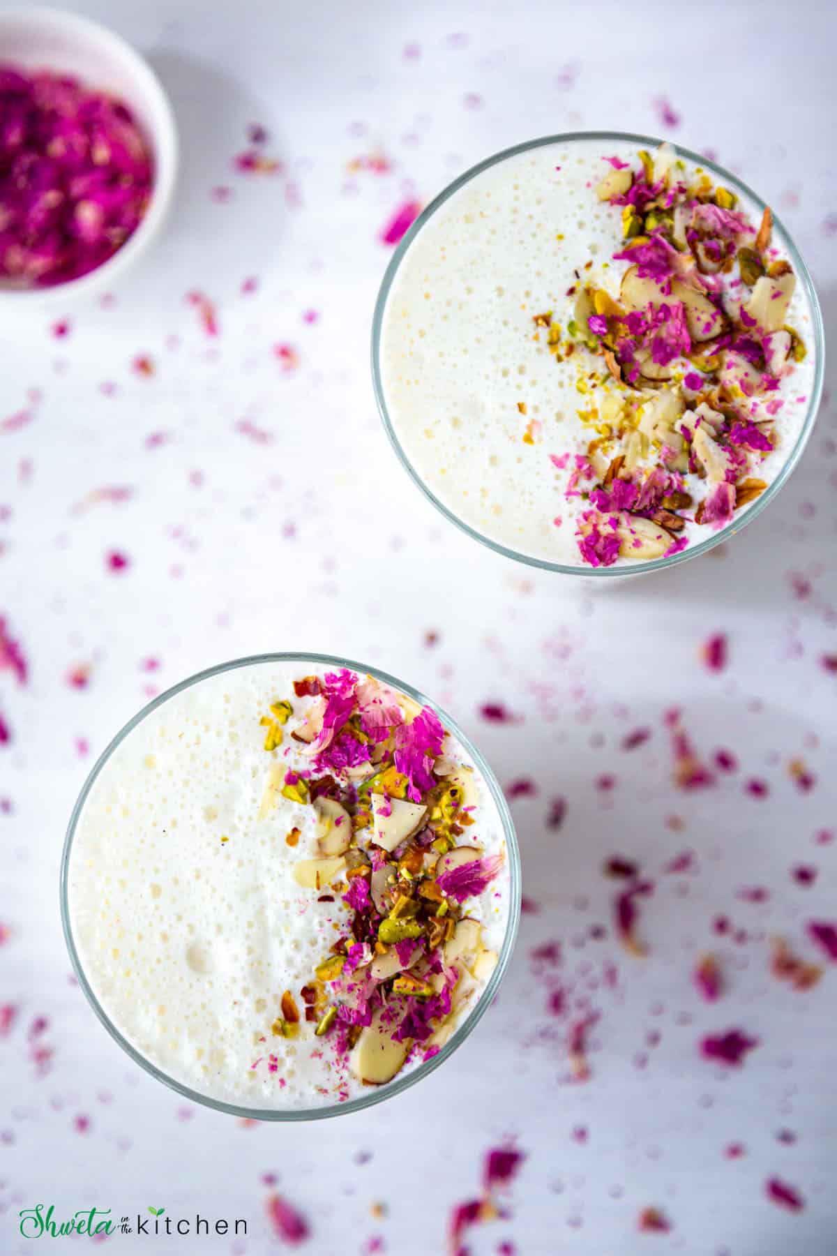 Top view of two glasses full of sweet lassi garnished with nuts and rose petals