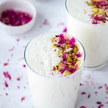 Two glass full of sweet lassi drink garnished with nuts and rose petals