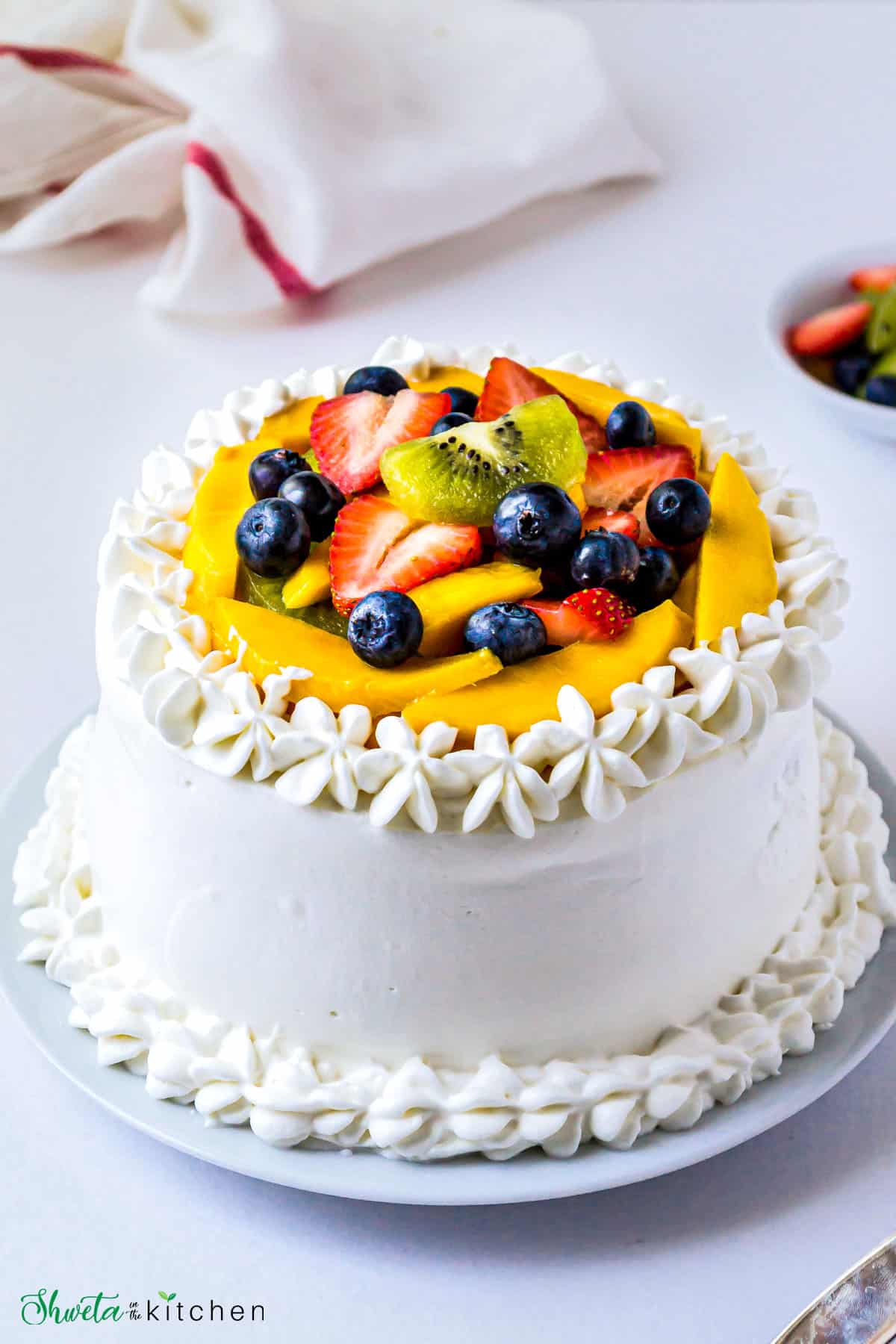 Layered Vanilla Sponge Cake frosted with Whipped Cream and topped with fresh fruits